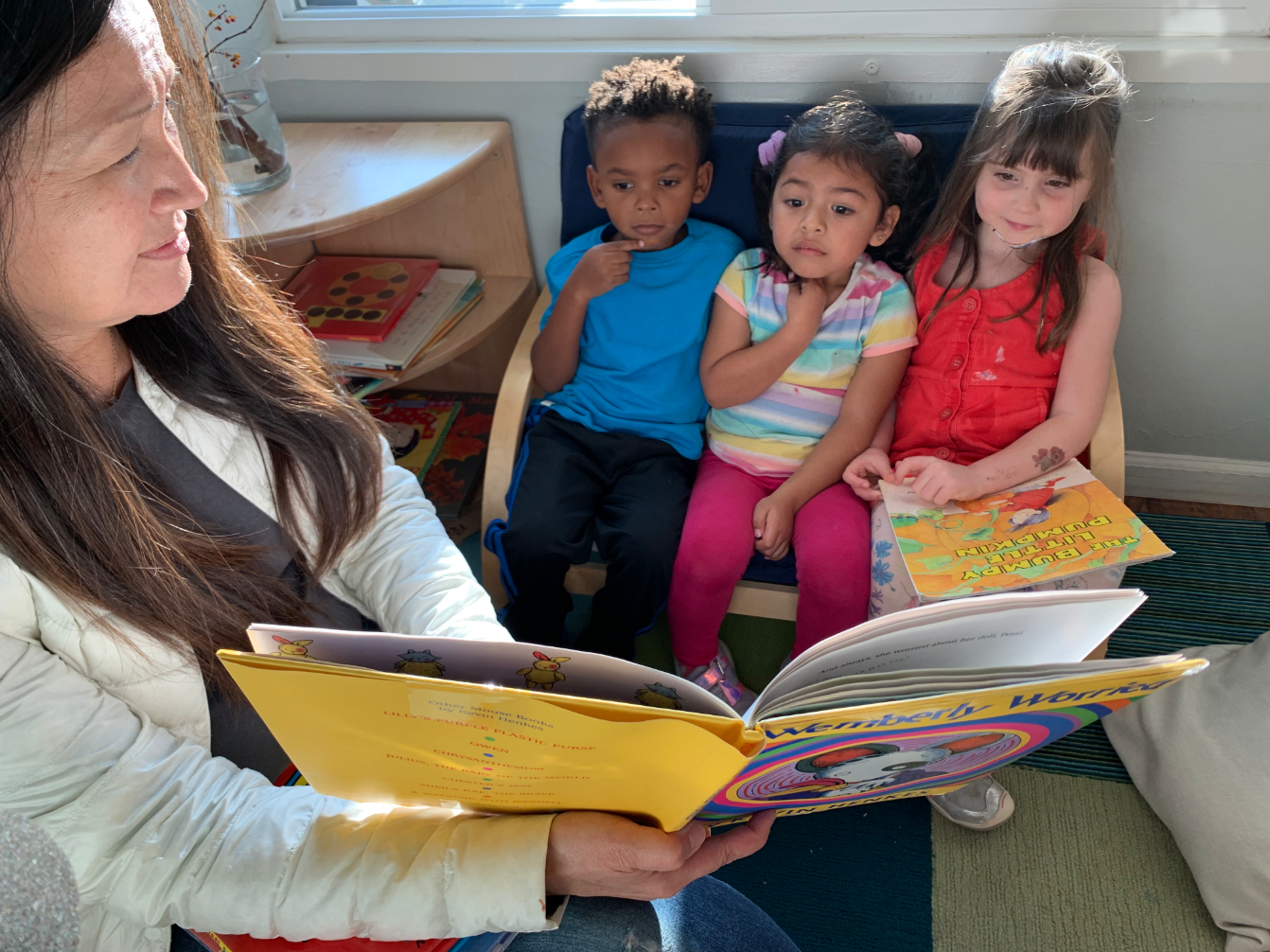 A teacher at All 5 preschool in East Menlo Park reads to children who have chosen book time after they woke up from their naps. All 5 preschool has integration as an explicit part of its mission, reserving half the seats for low-income children and the other half for middle and upper income children. (Deepa Fernandes for LAist)