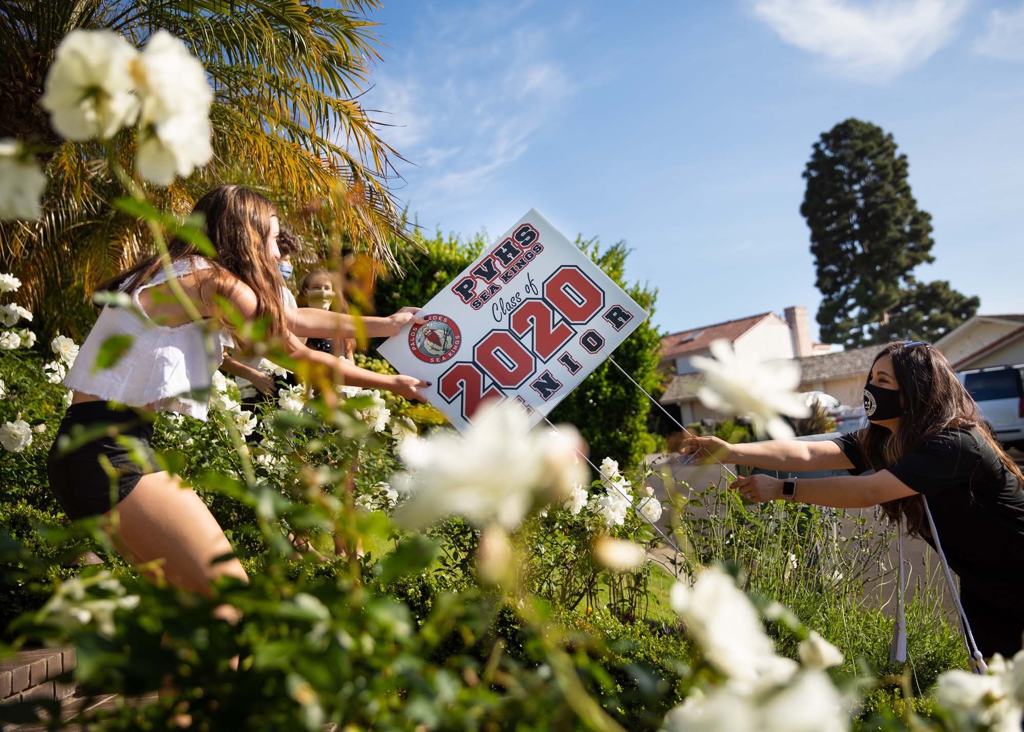 eacher Cynthia Mindicino (right) surprised her student Isabella Ruiz (left) at home with a yard sign celebrating her graduation. Palos Verdes High School teachers self-organized the effort to distribute the placards to all 400 seniors in the class, bargaining among themselves to visit specific graduates.