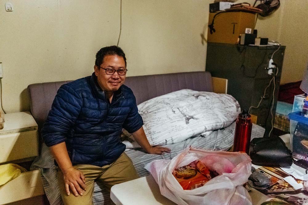 Zhang Chunsheng, a newly arrived immigrant from China, sits on the small futon he pays $15 a night for in a boarding house.
