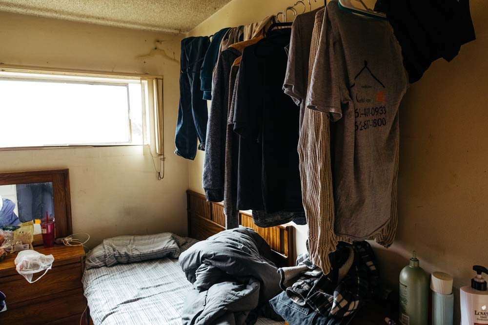 The shoes of multiple boarding house occupants. Tenants hang clothes above their beds.